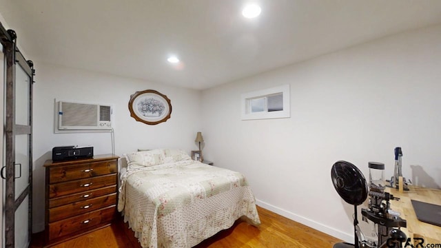 bedroom with a barn door, a wall mounted AC, and hardwood / wood-style floors