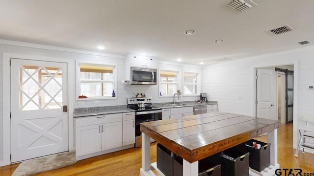 kitchen featuring sink, white cabinetry, stainless steel appliances, light hardwood / wood-style floors, and a barn door