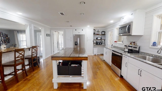 kitchen featuring sink, white cabinets, light hardwood / wood-style floors, stainless steel appliances, and crown molding