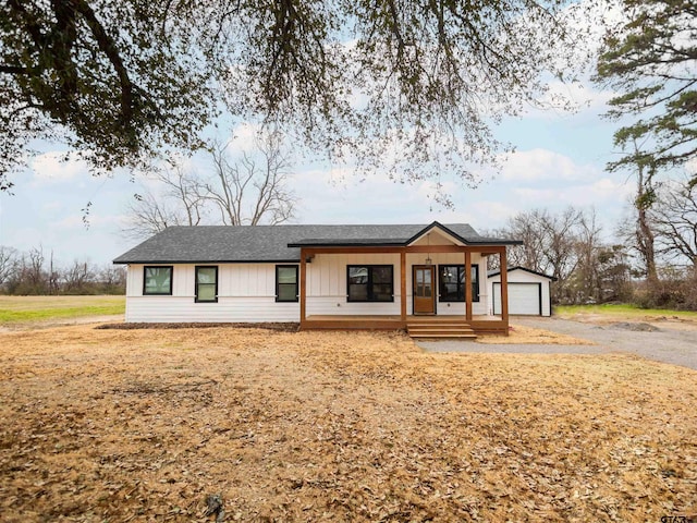 ranch-style house with roof with shingles, an outbuilding, a detached garage, covered porch, and aphalt driveway