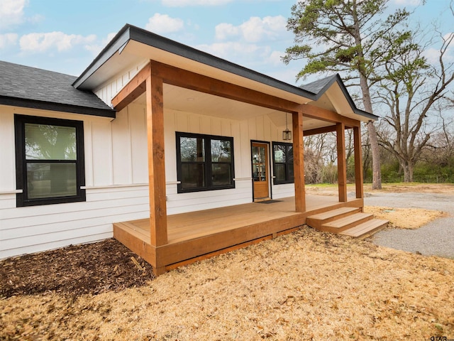 rear view of house featuring board and batten siding, a shingled roof, and covered porch