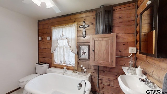 bathroom with wood walls, sink, ceiling fan, a bath, and toilet