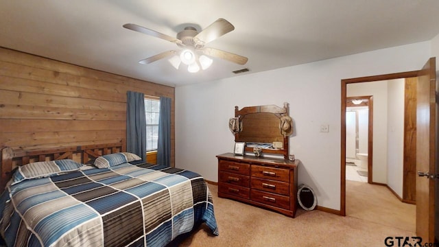 bedroom featuring ceiling fan, ensuite bath, wooden walls, and light colored carpet