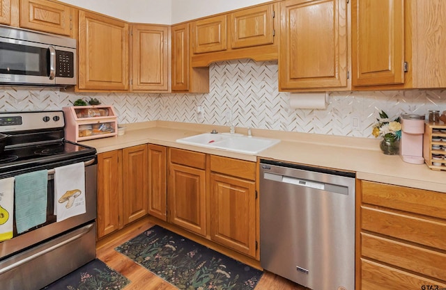 kitchen featuring stainless steel appliances, sink, decorative backsplash, and light hardwood / wood-style flooring