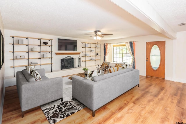 living room featuring ceiling fan, a textured ceiling, and light wood-type flooring