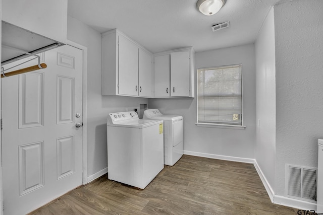 clothes washing area with washer and clothes dryer, cabinets, and wood-type flooring