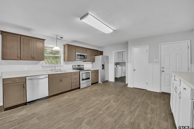 kitchen with sink, stainless steel appliances, hanging light fixtures, washer and dryer, and light wood-type flooring