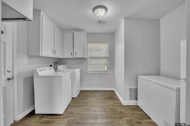 laundry area featuring dark hardwood / wood-style flooring, washer and clothes dryer, cabinets, and a textured ceiling