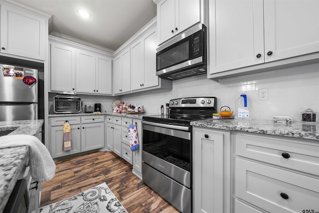 kitchen with stainless steel appliances, white cabinetry, tasteful backsplash, light stone countertops, and dark hardwood / wood-style flooring