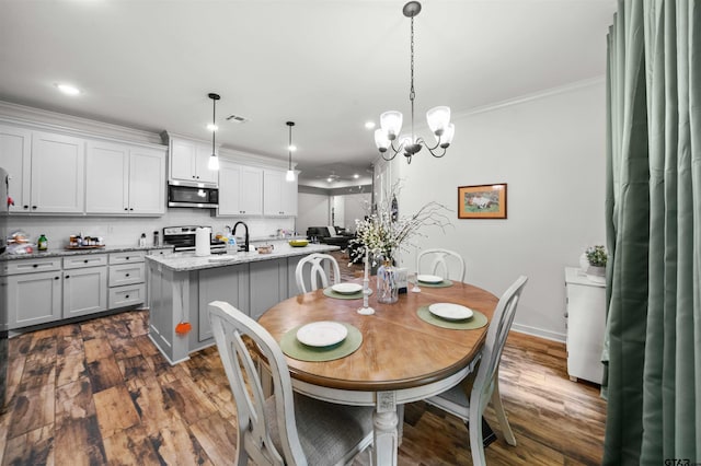 dining room featuring dark wood-type flooring, sink, an inviting chandelier, and ornamental molding