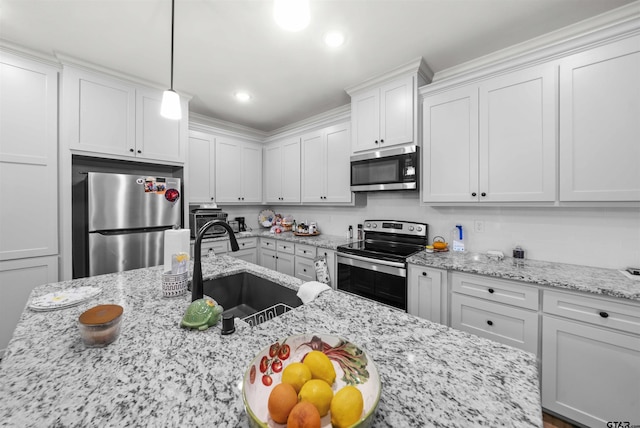 kitchen with white cabinetry, sink, light stone counters, appliances with stainless steel finishes, and pendant lighting