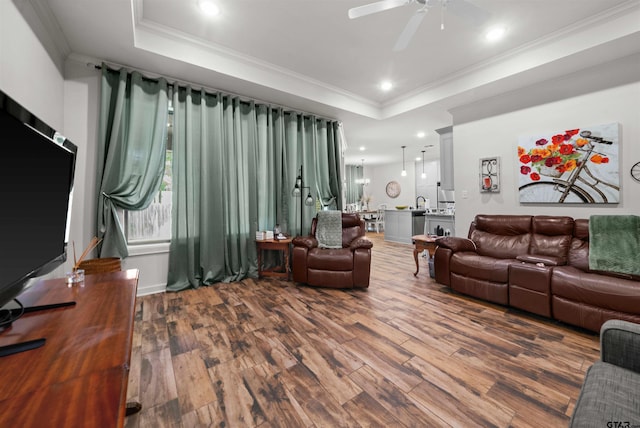 living room featuring ceiling fan, wood-type flooring, crown molding, and a tray ceiling