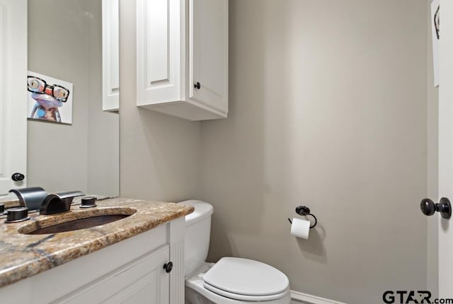 half bathroom with baseboards, vanity, and toilet