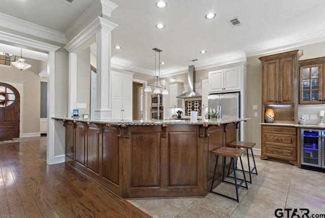 kitchen featuring wine cooler, stainless steel appliances, visible vents, wall chimney range hood, and glass insert cabinets