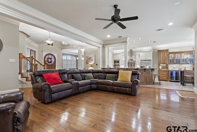 living area with beverage cooler, visible vents, light wood-style floors, stairs, and ornamental molding