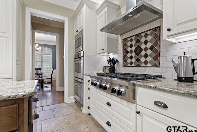 kitchen featuring light stone countertops, wall chimney range hood, appliances with stainless steel finishes, and white cabinetry