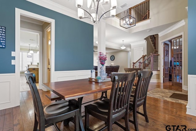 dining area featuring a wainscoted wall, ornamental molding, dark wood-type flooring, stairs, and a chandelier