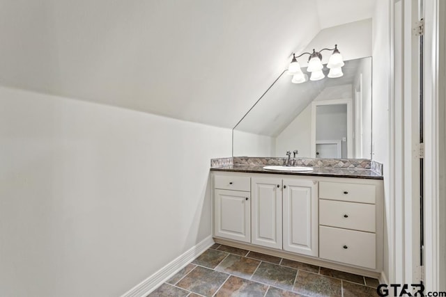 bathroom with stone finish flooring, vaulted ceiling, vanity, and baseboards