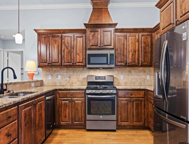 kitchen featuring stainless steel appliances, sink, light stone counters, crown molding, and light wood-type flooring