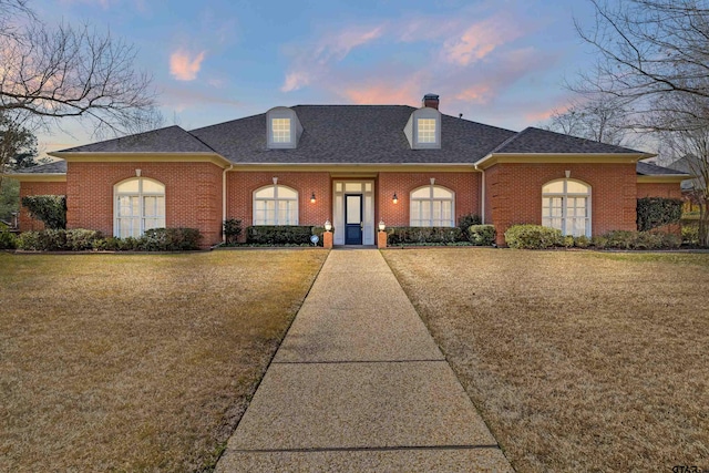 view of front of house with a chimney, a lawn, brick siding, and a shingled roof