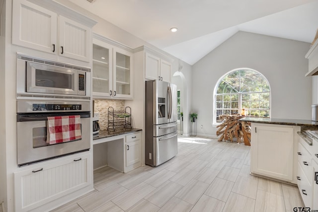 kitchen with appliances with stainless steel finishes, backsplash, dark stone counters, high vaulted ceiling, and white cabinetry