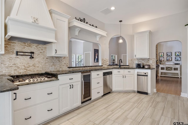 kitchen with custom exhaust hood, appliances with stainless steel finishes, decorative light fixtures, white cabinetry, and beverage cooler