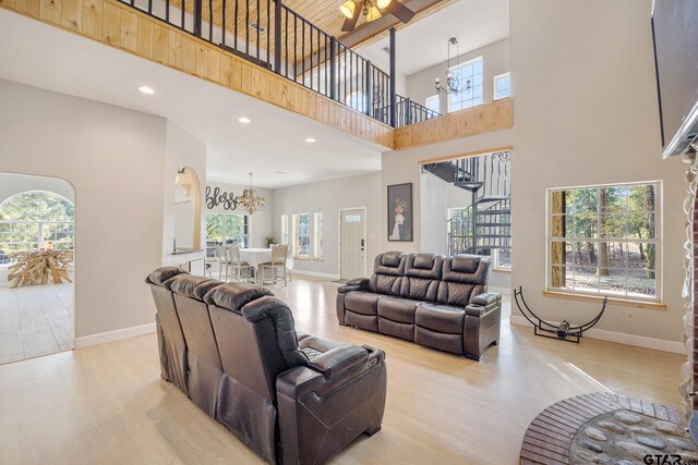 living room with a high ceiling, ceiling fan with notable chandelier, and light hardwood / wood-style flooring