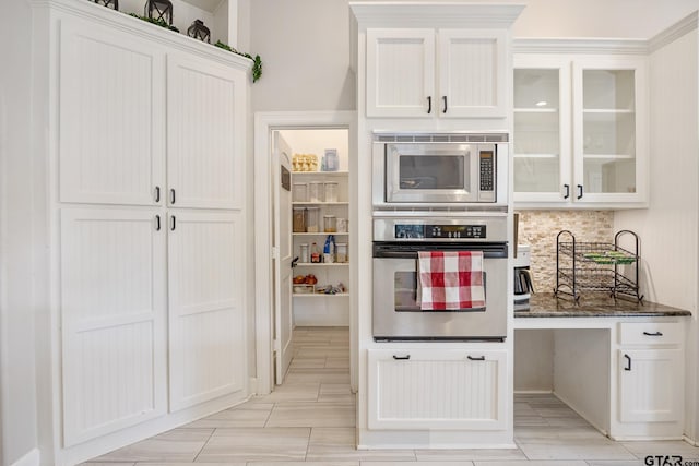 kitchen featuring white cabinets, dark stone countertops, built in desk, and appliances with stainless steel finishes