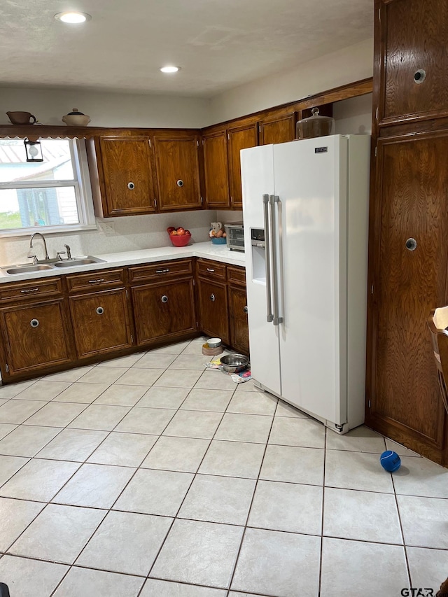 kitchen with light countertops, recessed lighting, white fridge with ice dispenser, a sink, and light tile patterned floors