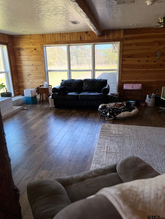 living area with hardwood / wood-style floors, visible vents, a textured ceiling, and wood walls