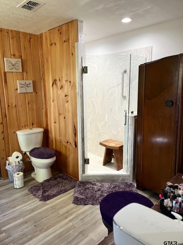 full bath featuring toilet, a shower stall, wooden walls, visible vents, and wood finished floors