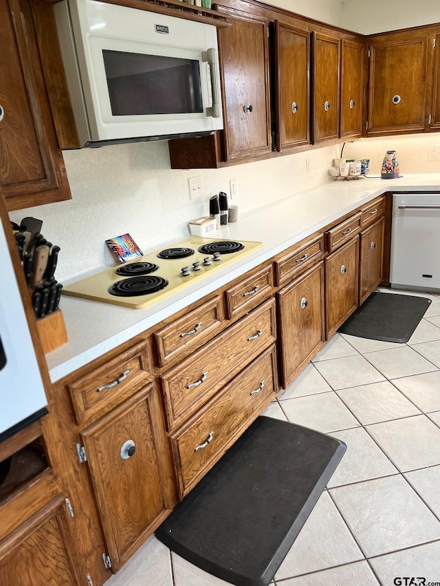 kitchen with light countertops, brown cabinetry, light tile patterned floors, and white appliances