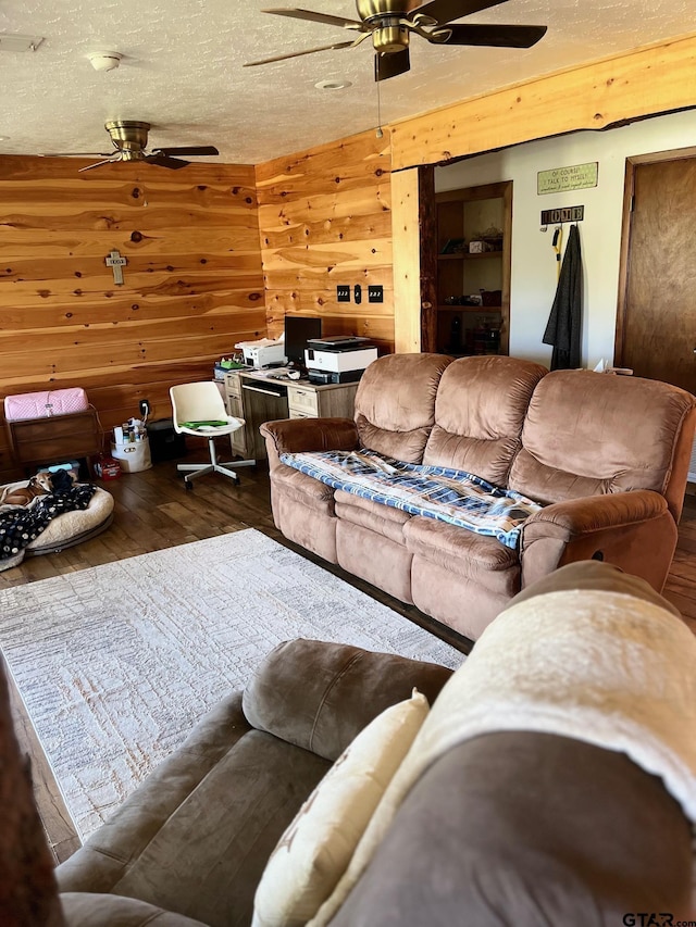 living area featuring a textured ceiling, ceiling fan, wood finished floors, and wood walls