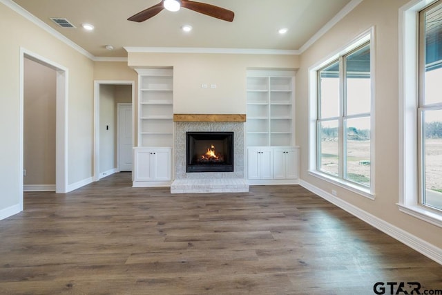 unfurnished living room featuring dark hardwood / wood-style floors, ceiling fan, built in shelves, ornamental molding, and a fireplace