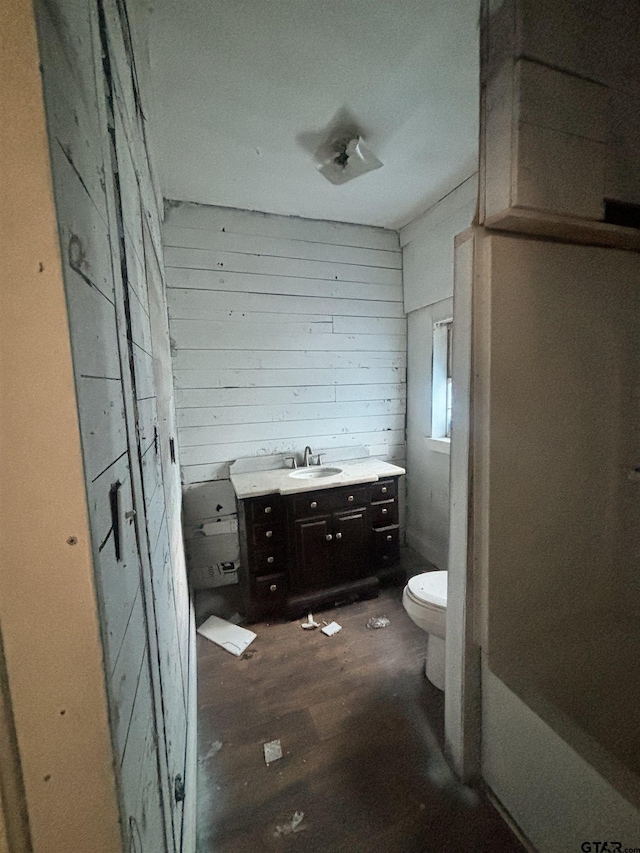 bathroom with hardwood / wood-style floors, vanity, wood walls, and toilet