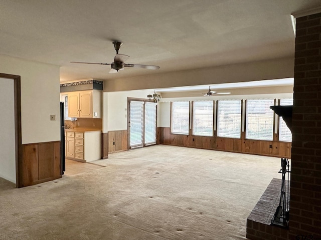 unfurnished living room with ceiling fan, wainscoting, wooden walls, and light colored carpet