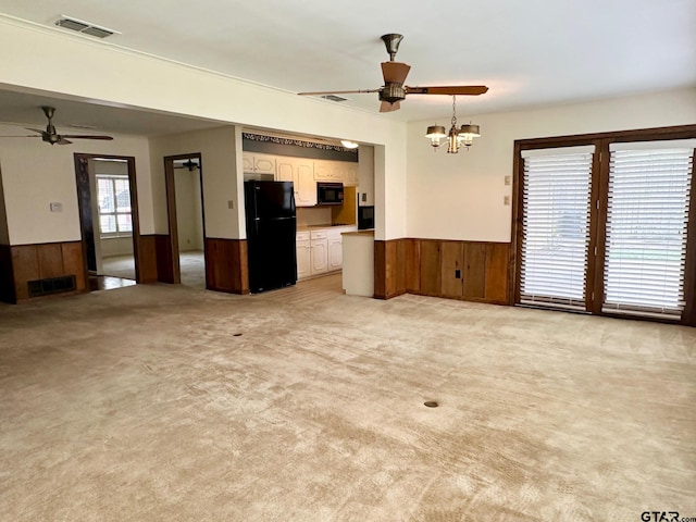 unfurnished living room featuring light carpet, ceiling fan with notable chandelier, and wooden walls