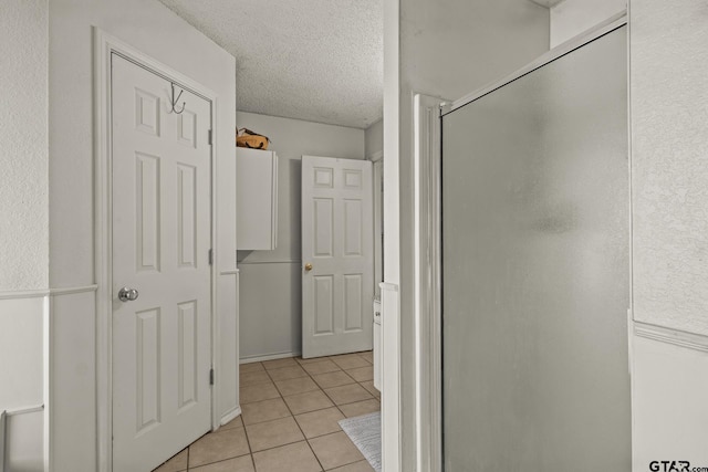 bathroom with tile patterned floors, a shower with door, and a textured ceiling