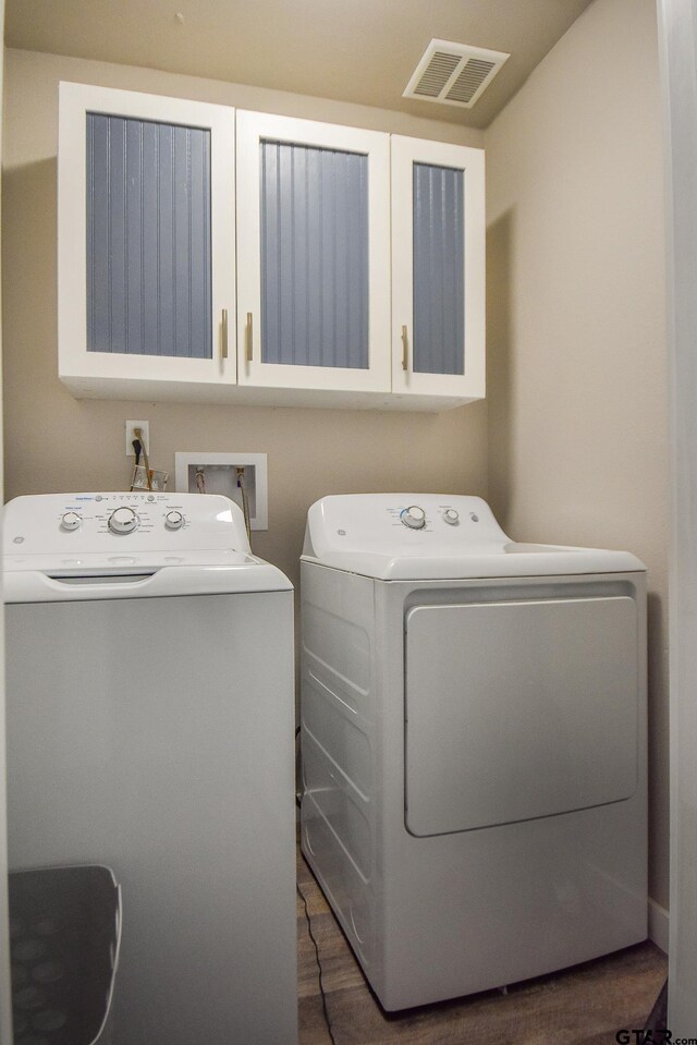 clothes washing area with washing machine and clothes dryer, dark hardwood / wood-style flooring, and cabinets