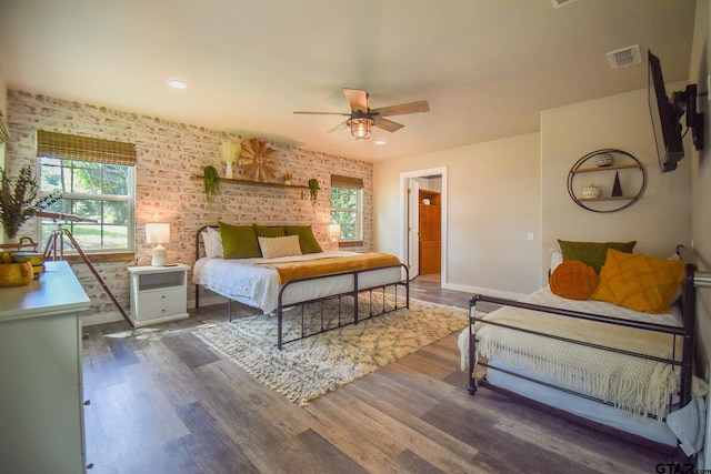 bedroom with dark hardwood / wood-style floors, ceiling fan, and brick wall