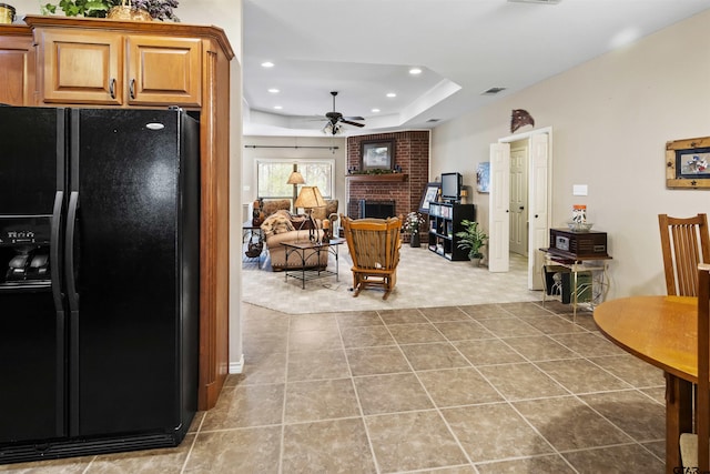 kitchen with visible vents, a brick fireplace, ceiling fan, black refrigerator with ice dispenser, and a raised ceiling