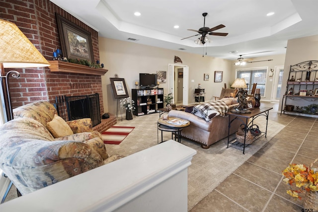 tiled living room featuring a tray ceiling, a brick fireplace, recessed lighting, and ceiling fan