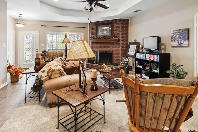 living room featuring light tile patterned floors, a ceiling fan, visible vents, a tray ceiling, and a fireplace