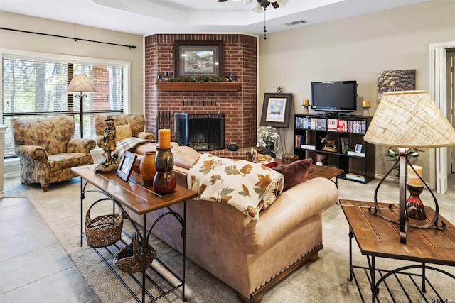 living area with visible vents, a brick fireplace, a tray ceiling, and ceiling fan