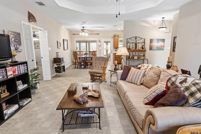 living area with light carpet, visible vents, a raised ceiling, and a ceiling fan