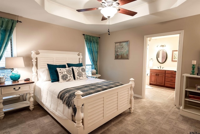 bedroom featuring connected bathroom, baseboards, ceiling fan, light colored carpet, and a raised ceiling