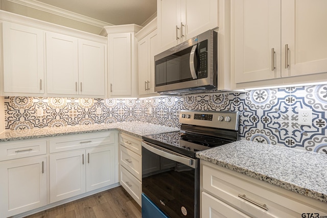 kitchen featuring tasteful backsplash, white cabinetry, light stone counters, stainless steel appliances, and crown molding