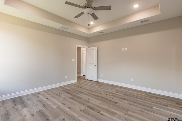 empty room with a raised ceiling, ceiling fan, and light hardwood / wood-style flooring