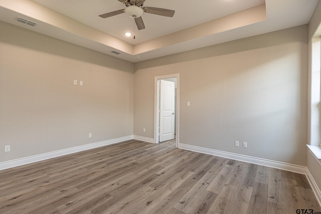 empty room featuring a raised ceiling, ceiling fan, and light hardwood / wood-style floors