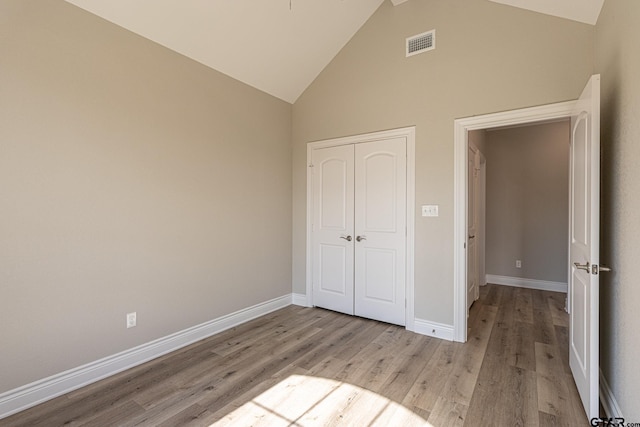 unfurnished bedroom with high vaulted ceiling, light hardwood / wood-style floors, and a closet